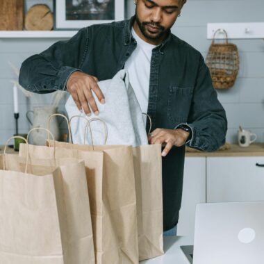 Adult man organizing purchases with paper bags and laptop in a modern home setting.