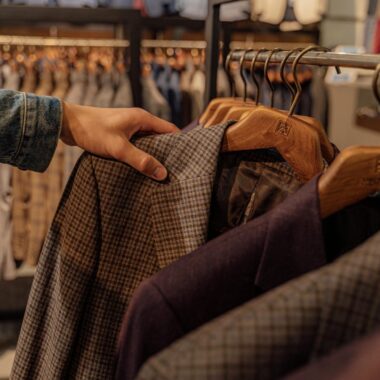 Close-up of a hand selecting men's blazers in a fashion store, highlighting trendy styles.