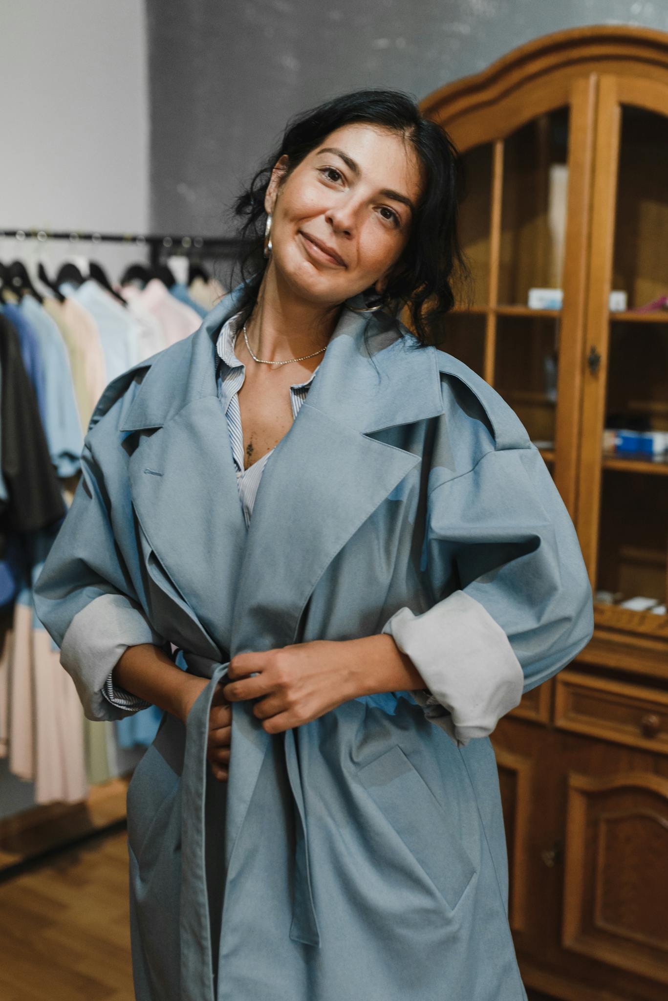 Woman in a stylish blue trench coat shopping in a trendy boutique. Indoor setting, fashion-focused.