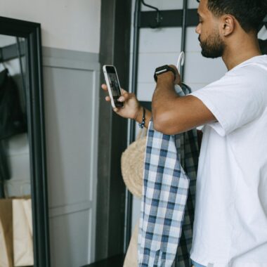Young man holding a plaid shirt and using smartphone for online shopping. Casual indoor setting.